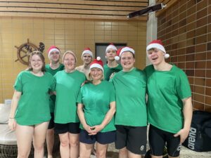 Ein Gruppenbild von Schwimmern vom TuS Finkenwerder. Sie tragen grüne Tshirts und Weihnachtsmützen.