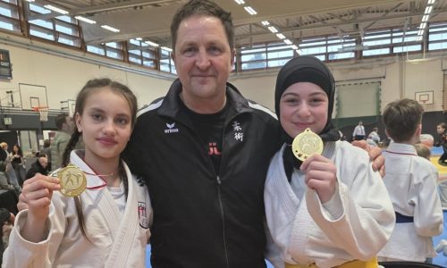 3 Personen, zwei Jugendliche mit ihren Medaillen und der Trainer in der Mitte