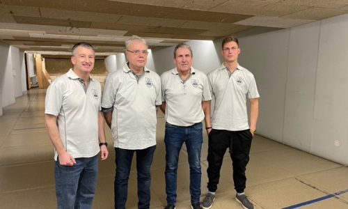 Vier Männer stehen an einem Schießstand und lächeln in die Kamera.