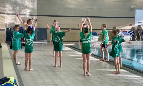 Eine Gruppe von jungen Athletinnen und Athleten stehen im Kreis und machen Aufwärmübungen um an einem Schwimmwettkampf teilzunehmen.