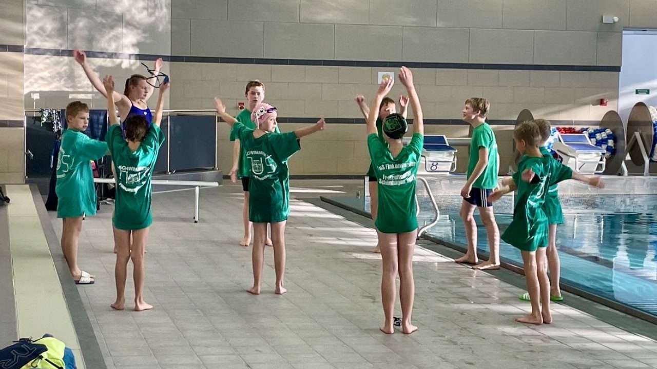 Eine Gruppe von jungen Athletinnen und Athleten stehen im Kreis und machen Aufwärmübungen um an einem Schwimmwettkampf teilzunehmen.